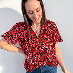 Woman wearing a red and black patterned blouse and blue jeans against a light gray background