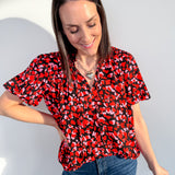 Woman wearing a red and black patterned blouse and blue jeans against a light gray background
