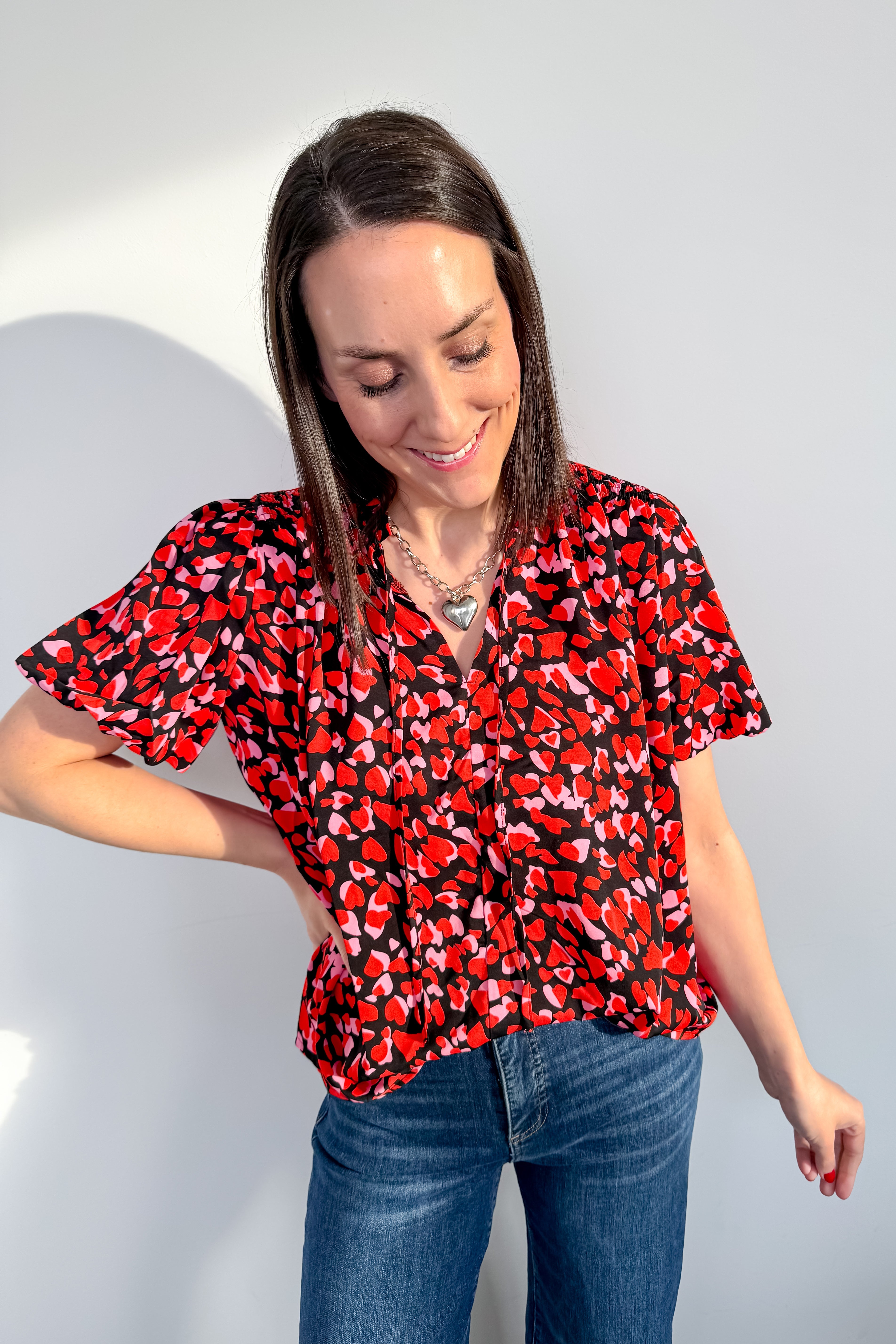 Woman wearing a red and black patterned blouse and blue jeans against a light gray background