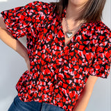 Woman wearing a red and black patterned blouse with blue jeans against a light background