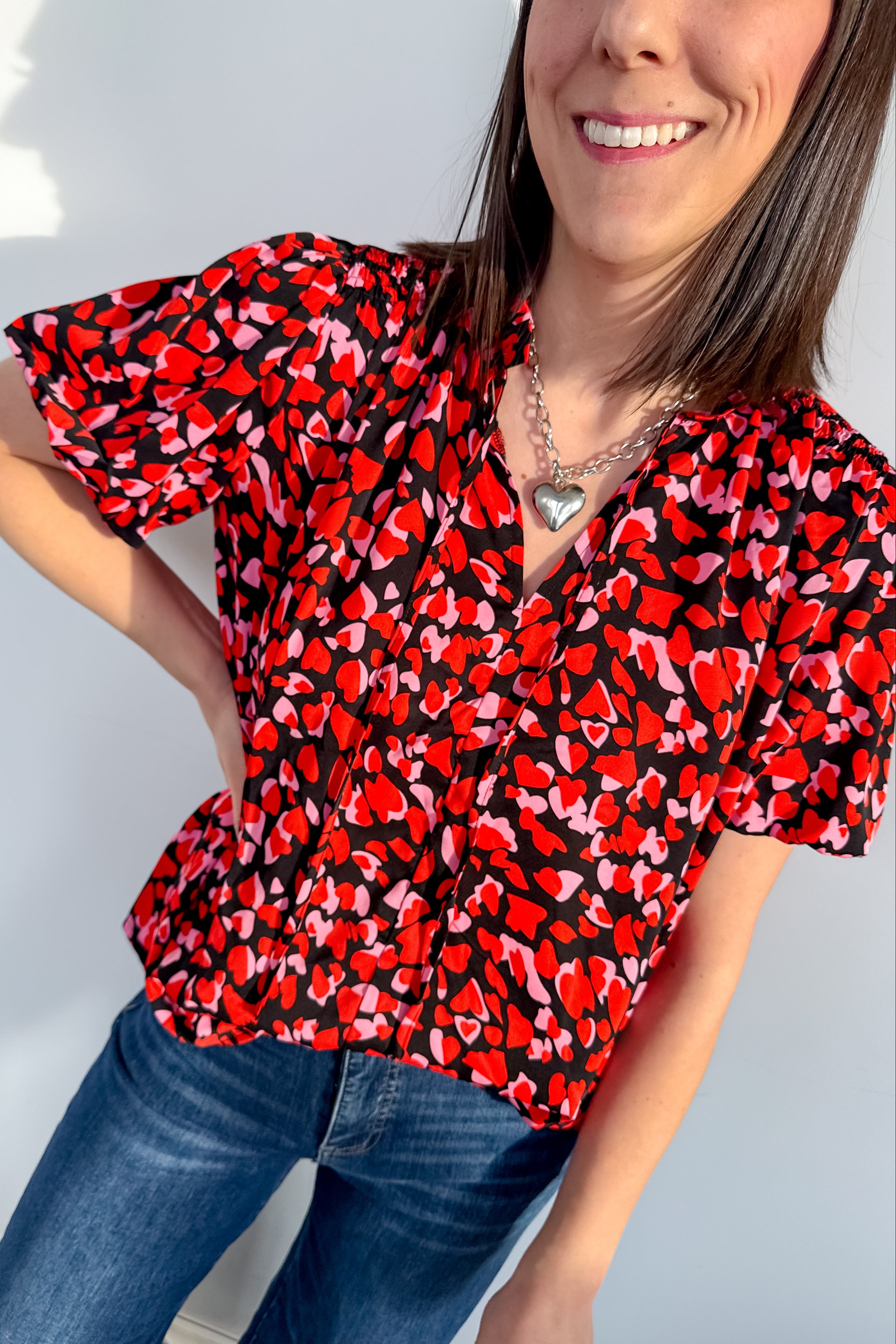 Woman wearing a red and black patterned blouse with blue jeans against a light background