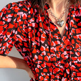 Person wearing a red and black patterned blouse with a heart necklace against a light background