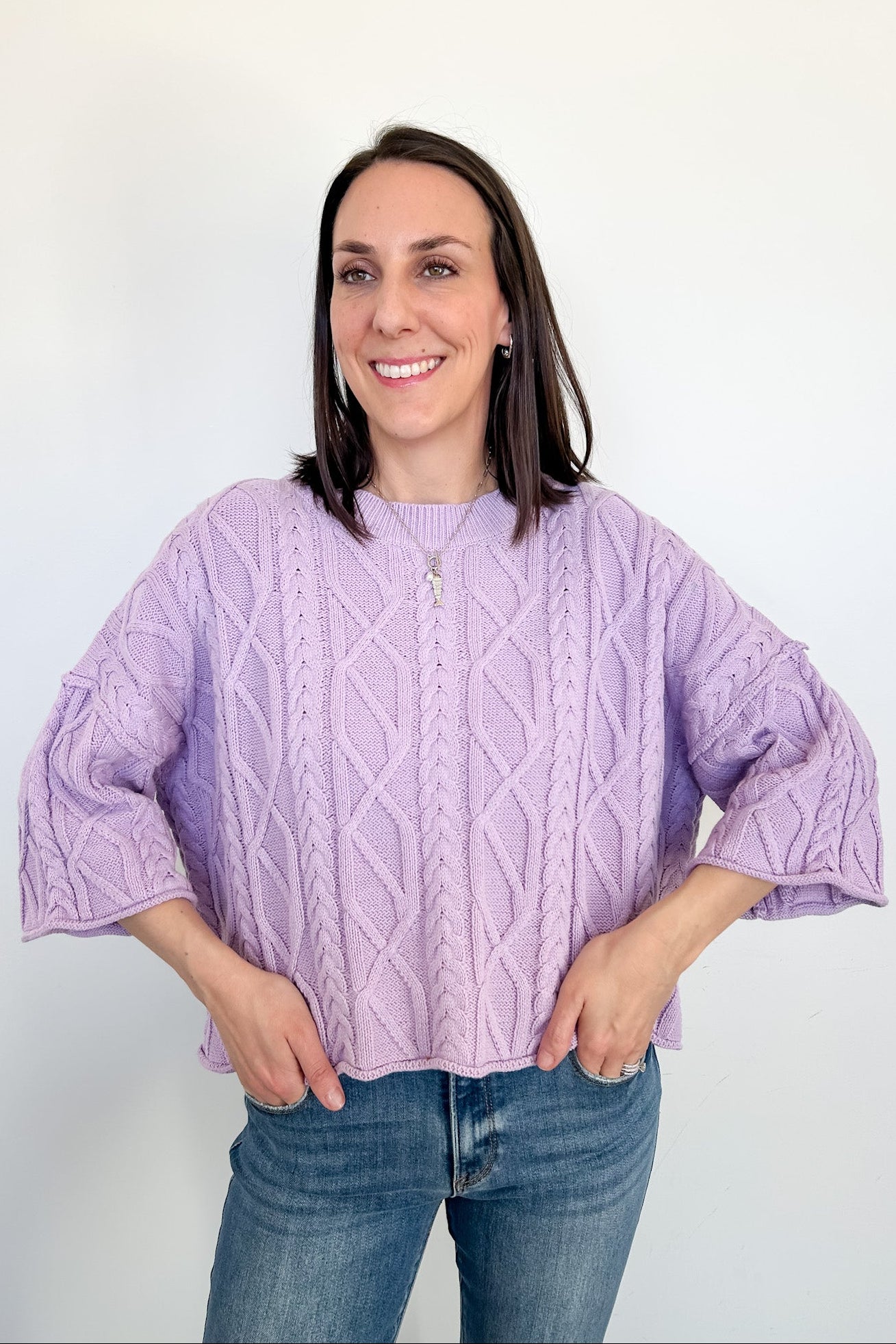 Woman wearing a purple cable knit sweater against a white background