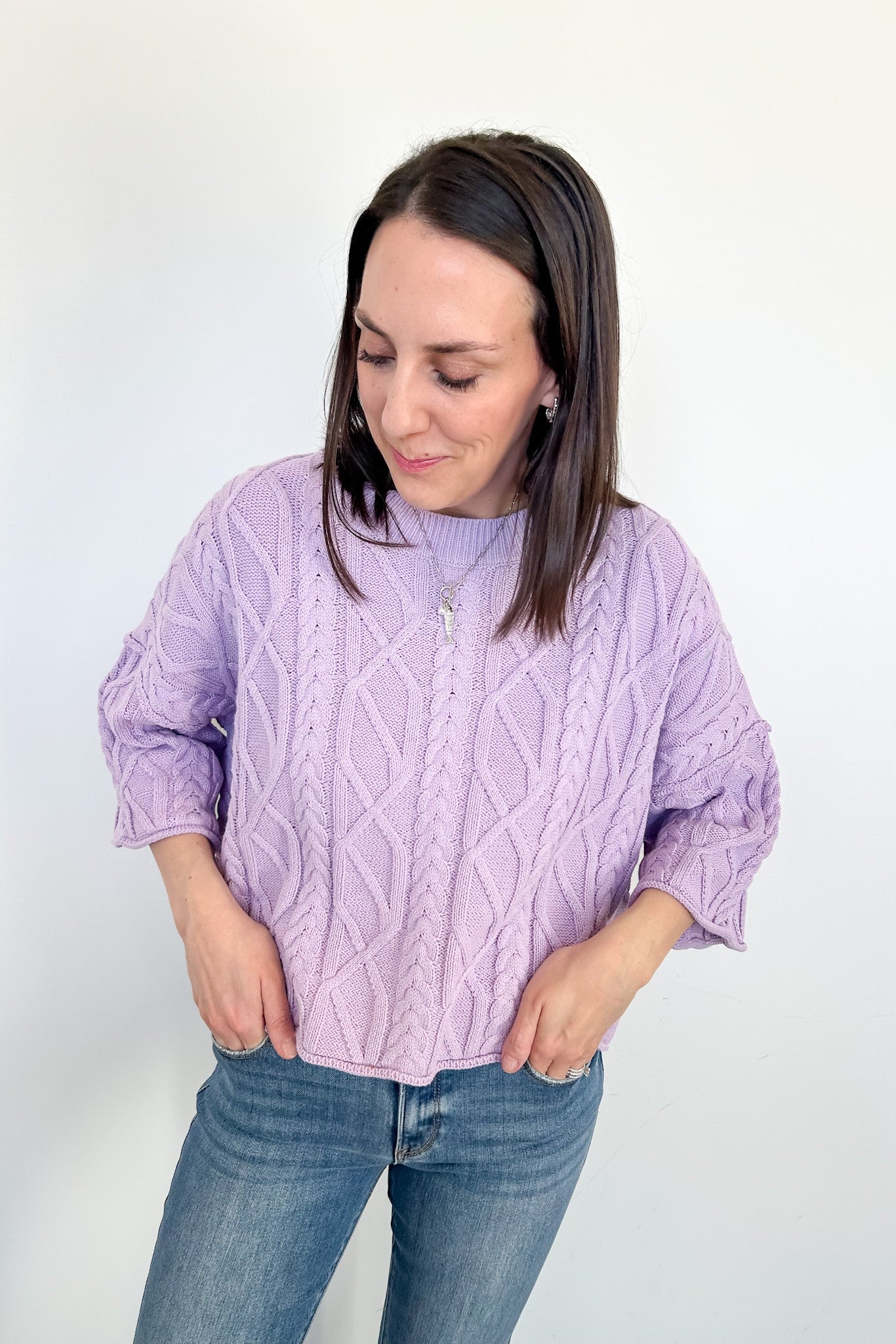 Woman wearing a purple cable knit sweater and blue jeans on a white background