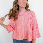Woman wearing a pink cable knit sweater and blue jeans against a white background
