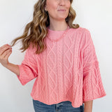 Woman wearing a pink cable knit sweater and blue jeans against a white background