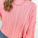 Person wearing a pink cable knit sweater and blue jeans on a white background
