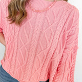 Person wearing a pink cable knit sweater and blue jeans on a white background