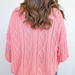 Person wearing a pink cable knit sweater against a white background