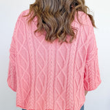 Person wearing a pink cable knit sweater against a white background