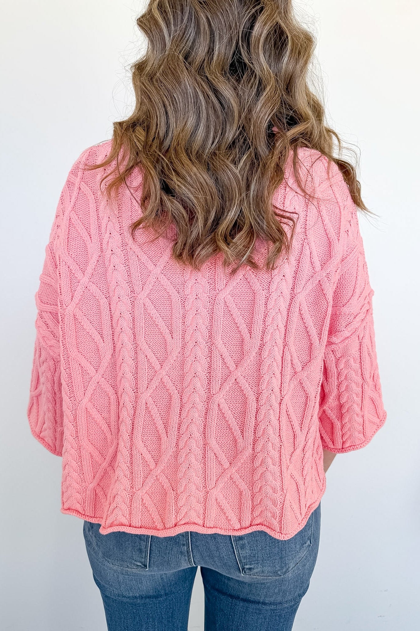 Person wearing a pink cable knit sweater against a white background