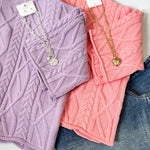 Two sweaters, one purple and one pink, with jewelry on a white background.