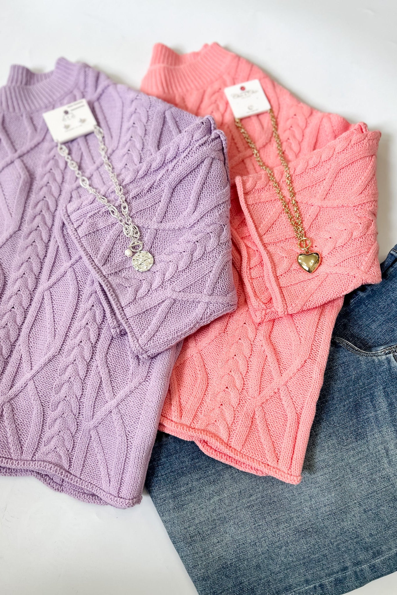 Two sweaters, one purple and one pink, with jewelry on a white background.