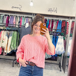 Person taking a mirror selfie wearing a pink sweater and blue jeans in a clothing store.