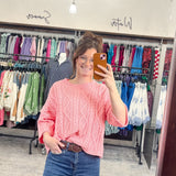 Person taking a mirror selfie wearing a pink sweater and blue jeans in a clothing store.