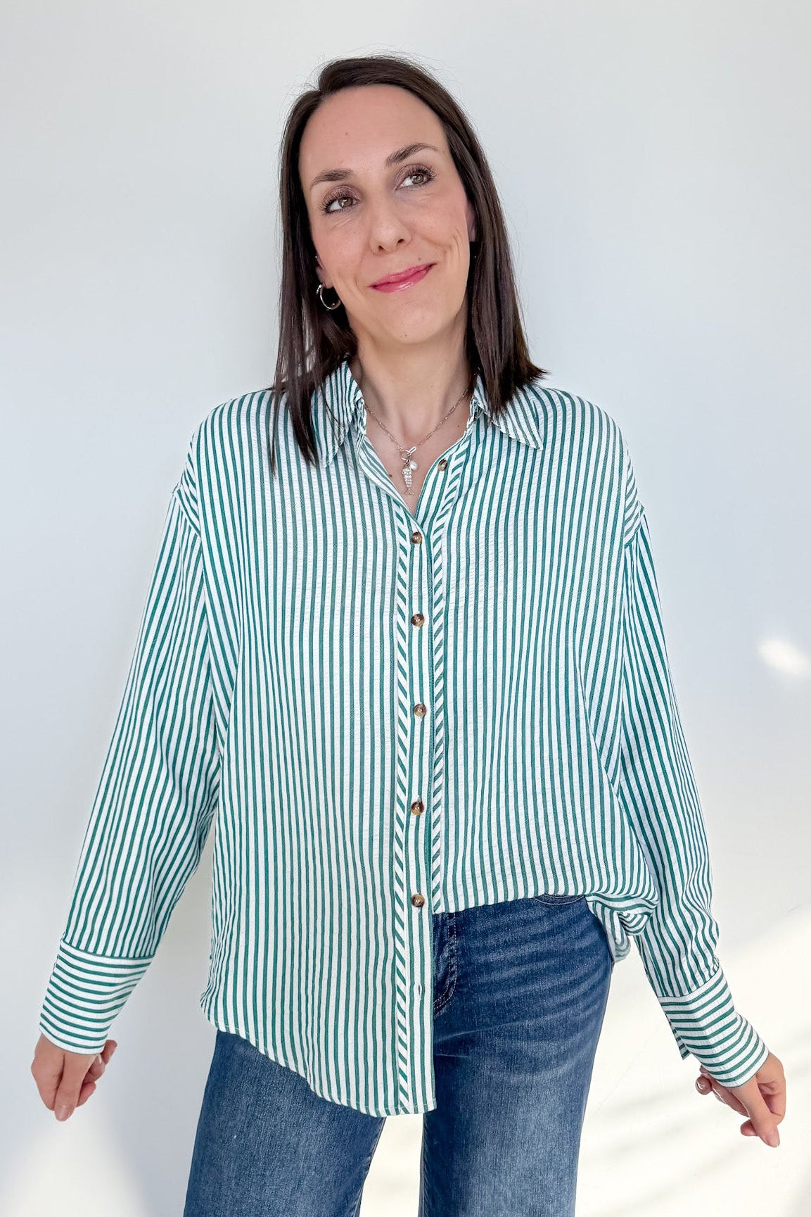 Woman wearing a green and white striped shirt and blue jeans against a white background