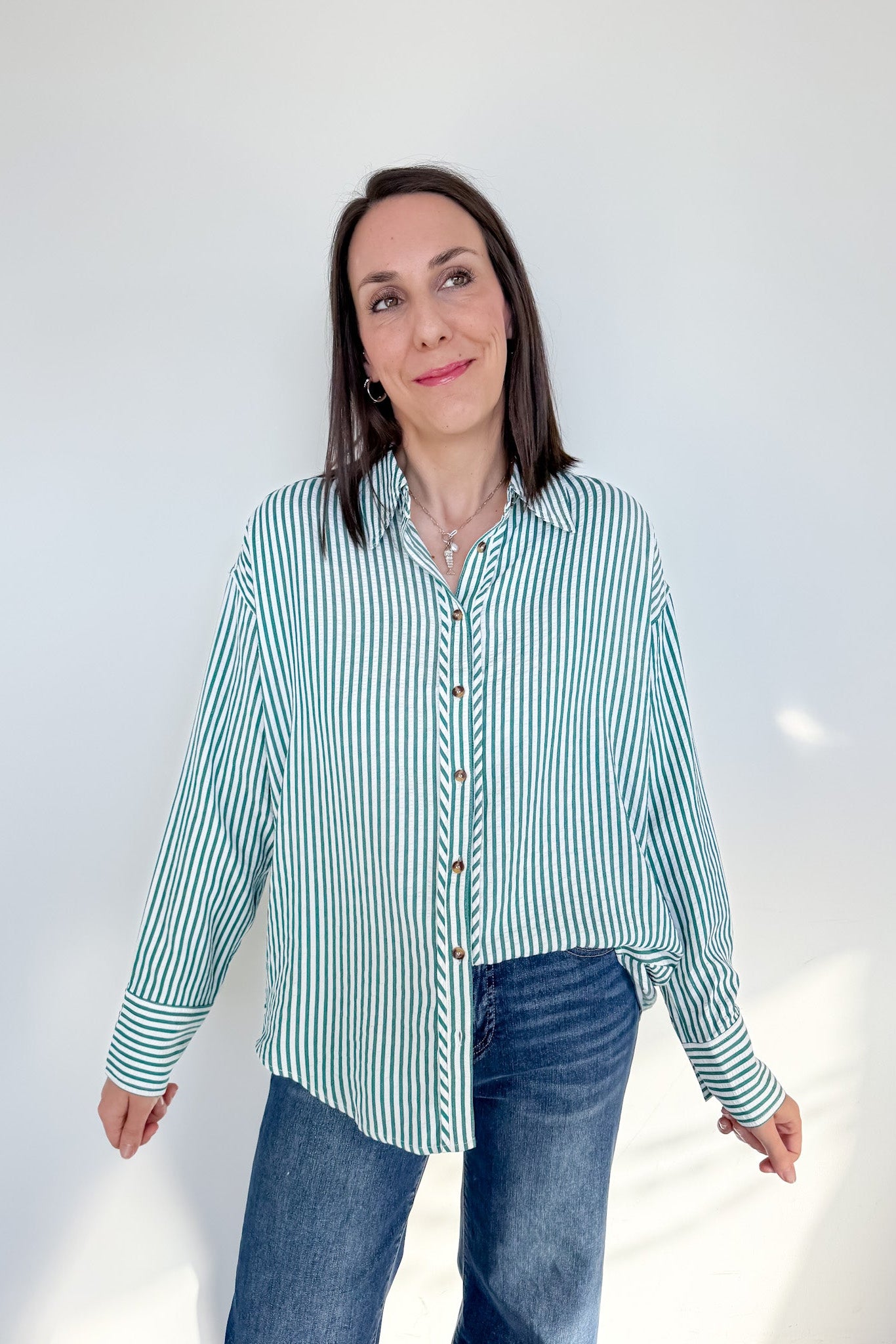 Woman wearing a green and white striped shirt and blue jeans against a white background
