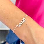 Silver bracelet with 'WWJD' on a wrist against a pink and blue background