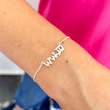 Silver bracelet with 'WWJD' on a wrist against a pink and blue background
