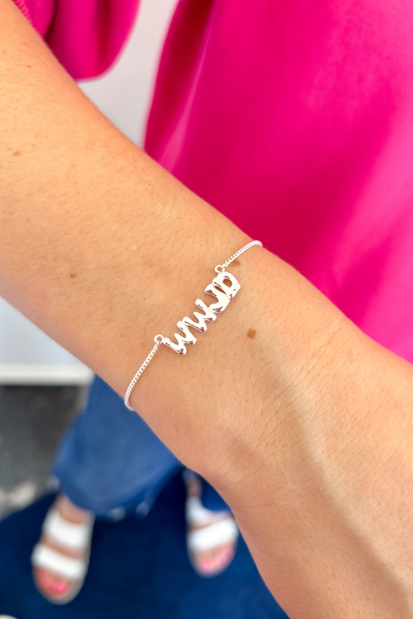 Silver bracelet with 'WWJD' on a wrist against a pink and blue background