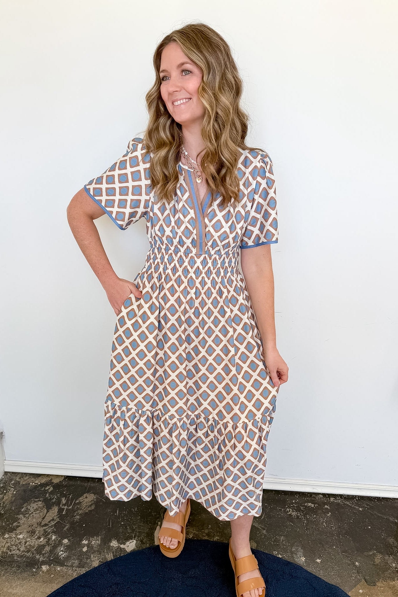 Woman wearing a patterned dress standing against a white wall.