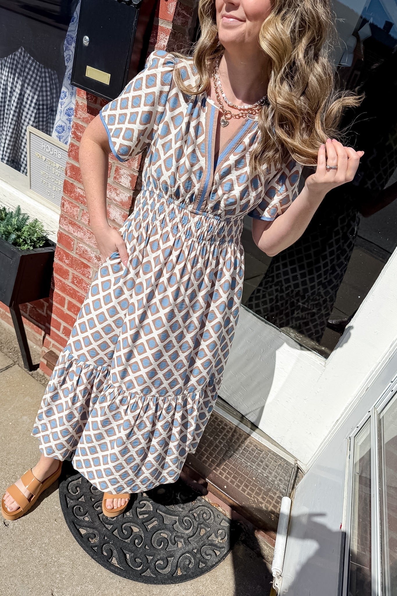 Woman in a patterned dress standing on a step outside a building.