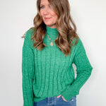Woman wearing a green sweater and blue jeans against a white background