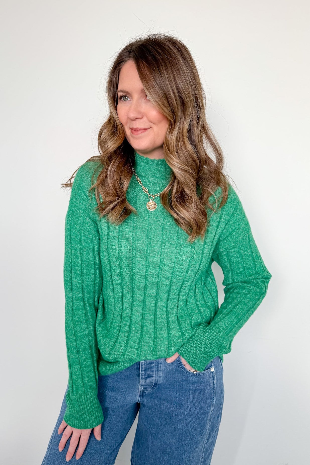 Woman wearing a green sweater and blue jeans against a white background
