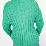 Green sweater worn by a person against a white wall