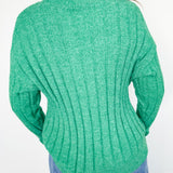 Green sweater worn by a person against a white wall