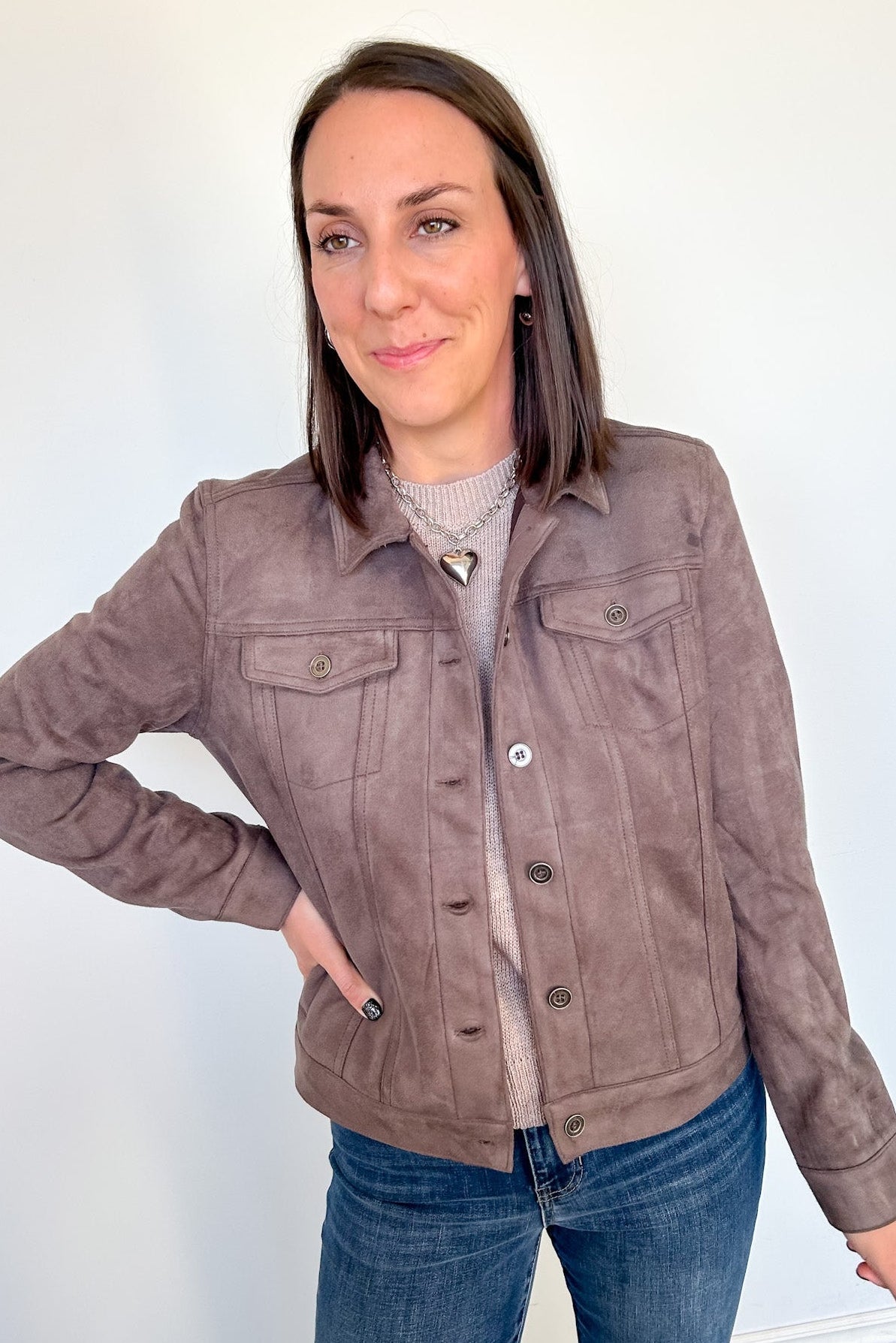 Woman wearing light brown jacket with her hand on her hip.