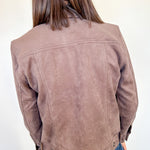 Person wearing a brown suede jacket against a white wall