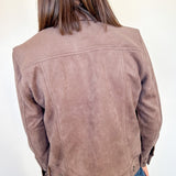 Person wearing a brown suede jacket against a white wall