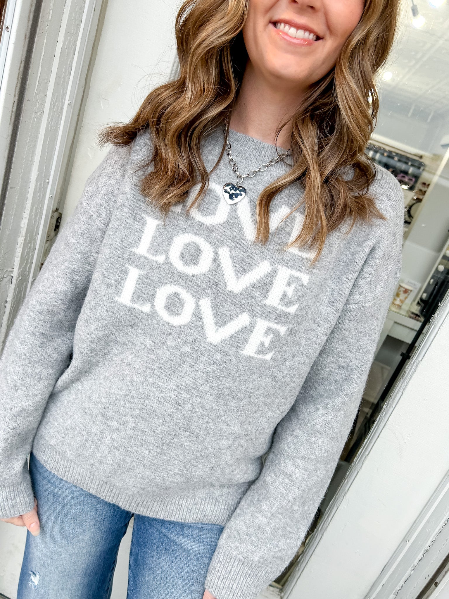 Person wearing a gray sweater with 'LOVE' text, standing indoors.