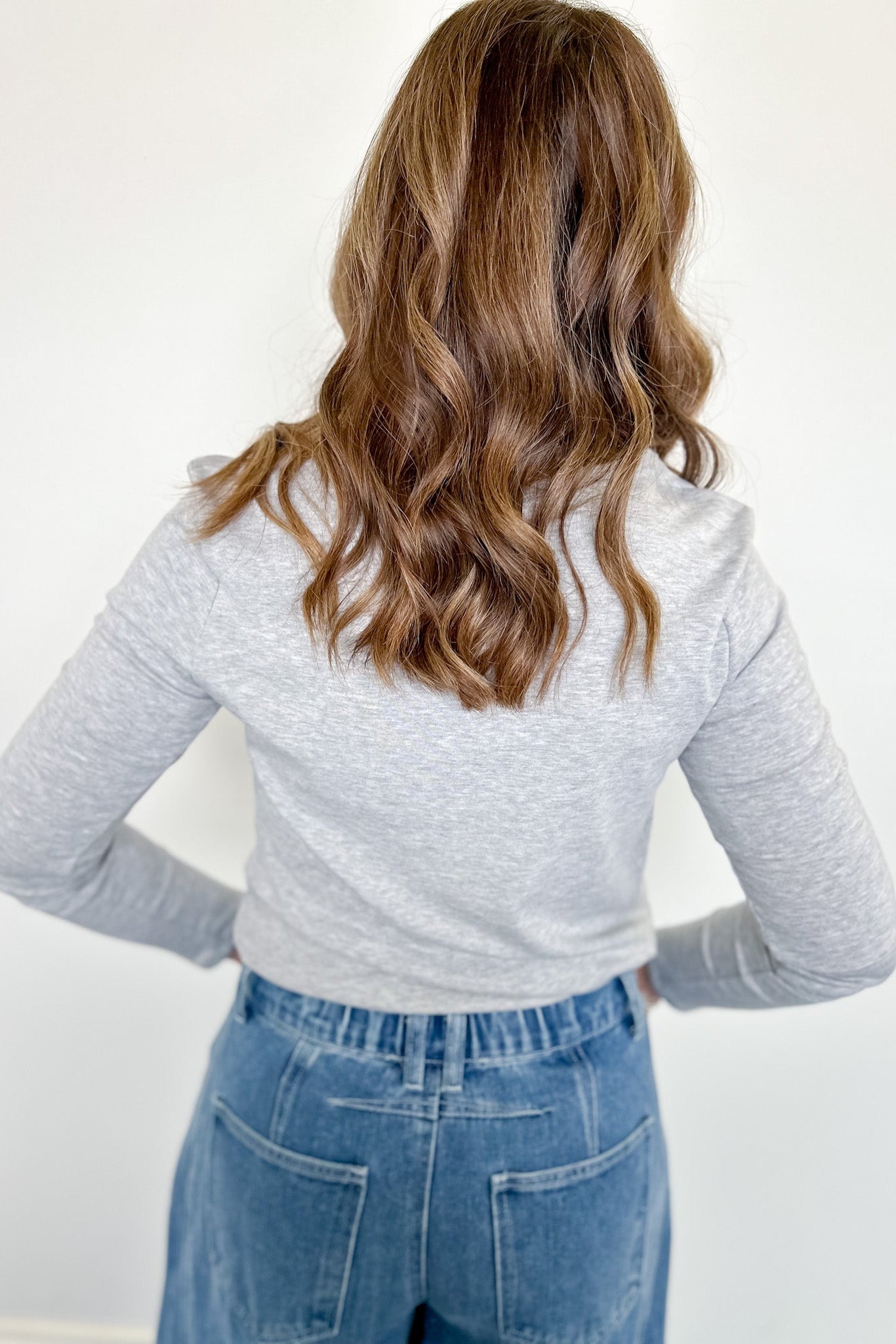 Person wearing a gray long-sleeve top and blue jeans with a plain white background