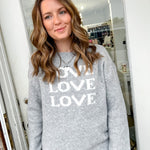 Woman wearing a gray sweatshirt with 'LOVE' printed on it, standing in front of a mirror.