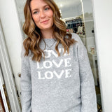 Woman wearing a gray sweatshirt with 'LOVE' printed on it, standing in front of a mirror.