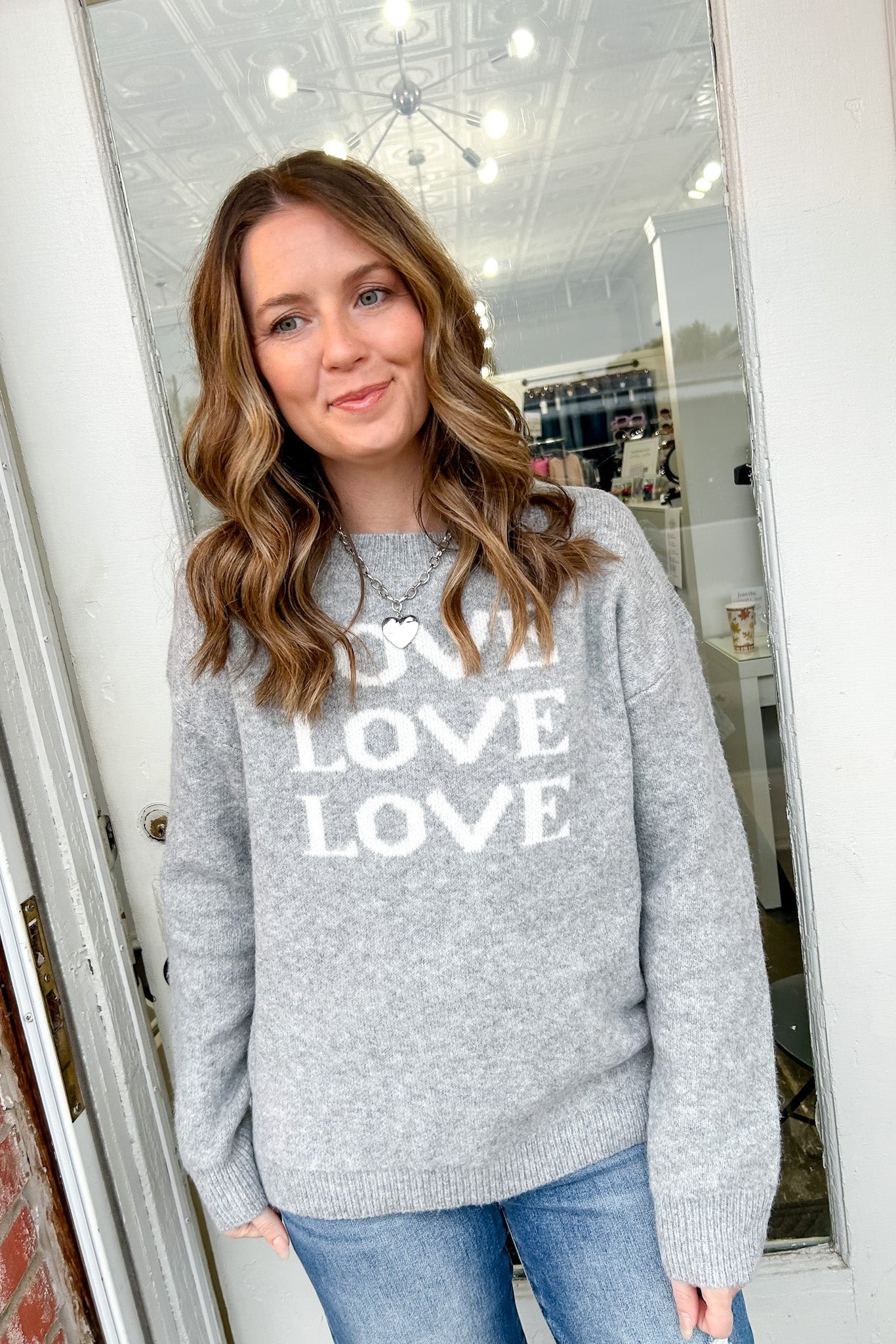 Woman wearing a gray sweatshirt with 'LOVE' printed on it, standing in front of a mirror.