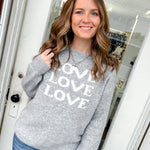 Woman wearing a gray sweater with 'LOVE' print, standing in front of a door frame