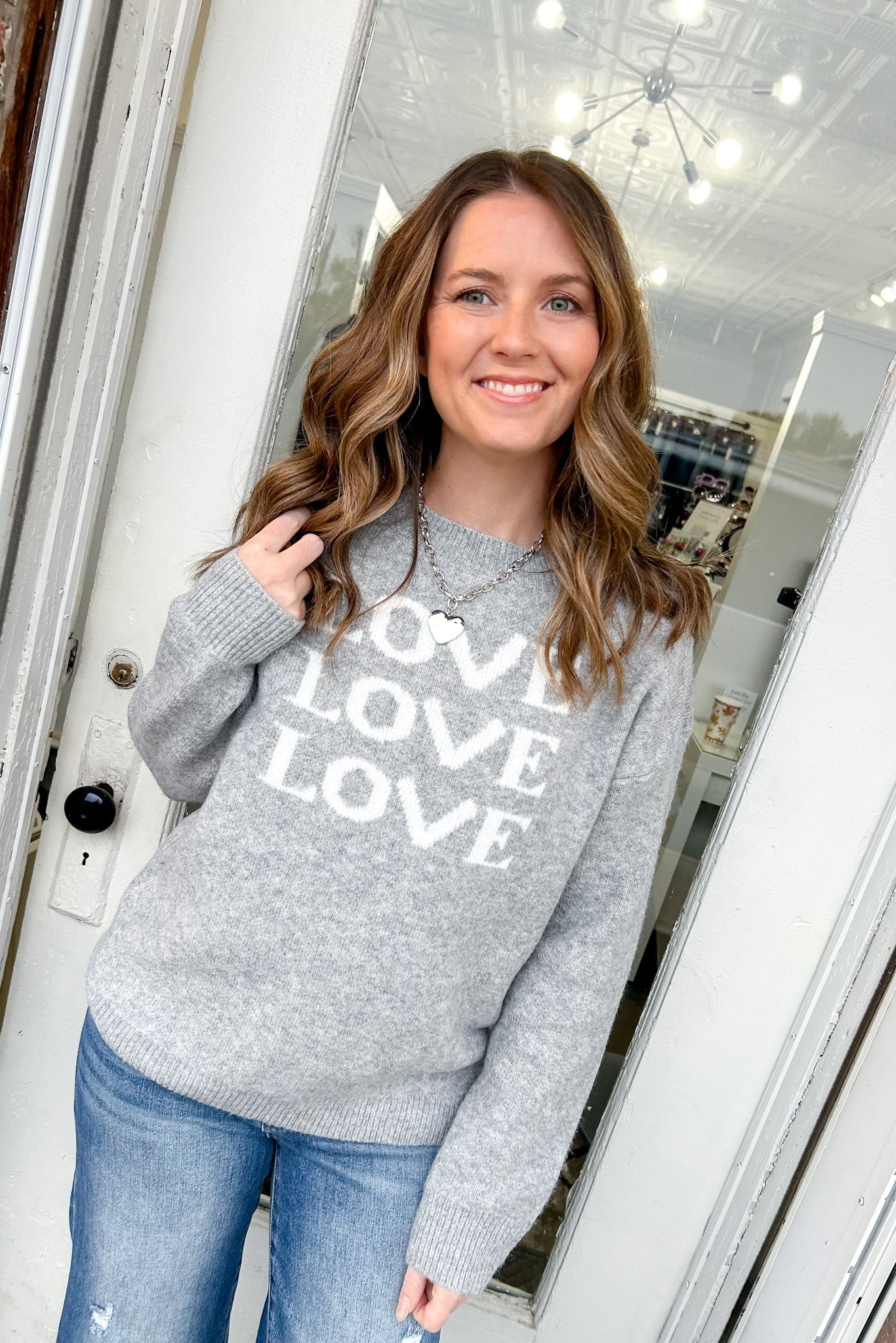 Woman wearing a gray sweater with 'LOVE' print, standing in front of a door frame