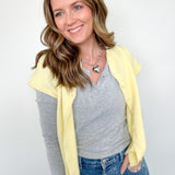 Woman wearing a yellow cardigan, gray shirt, and blue jeans against a white background