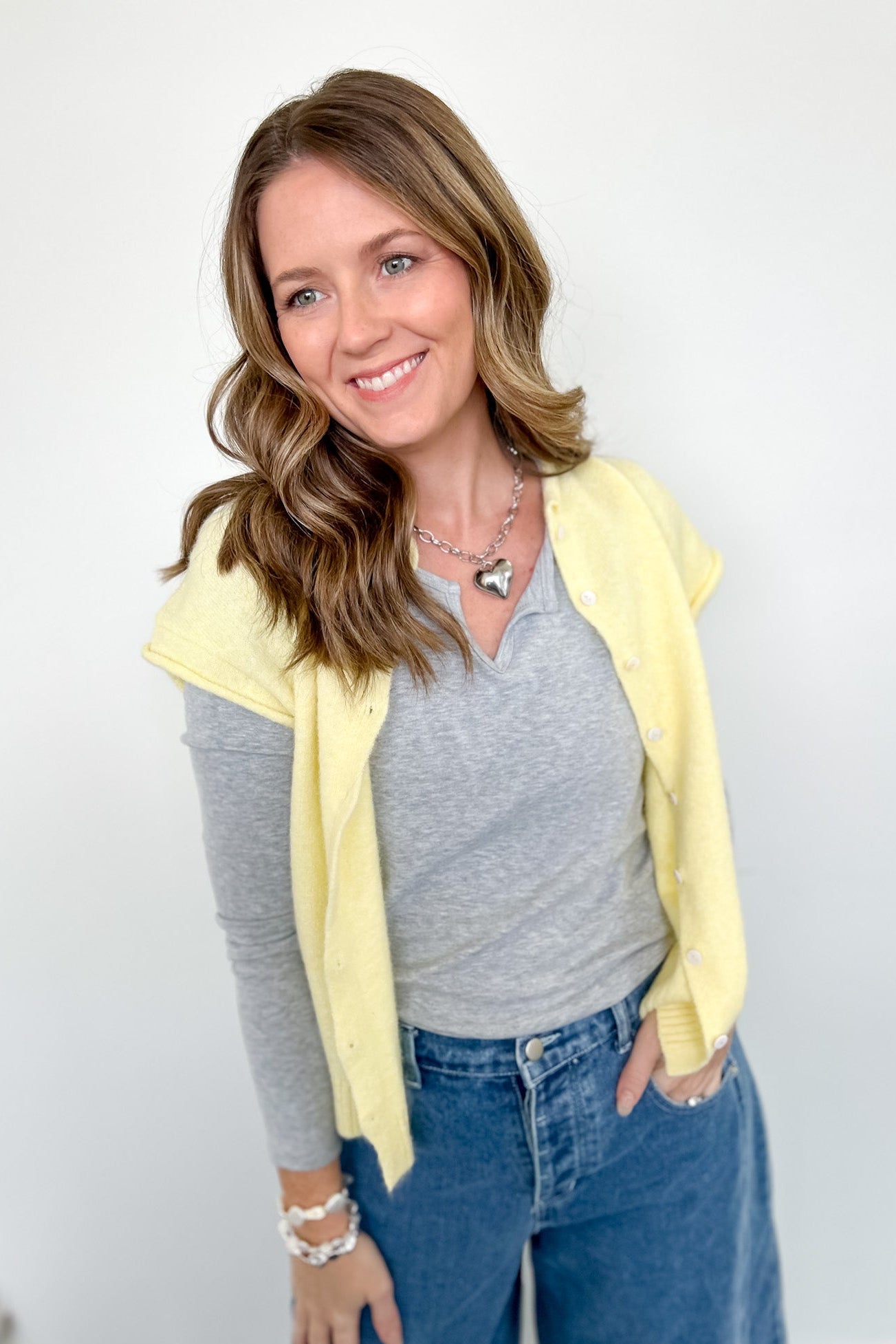 Woman wearing a yellow cardigan, gray shirt, and blue jeans against a white background