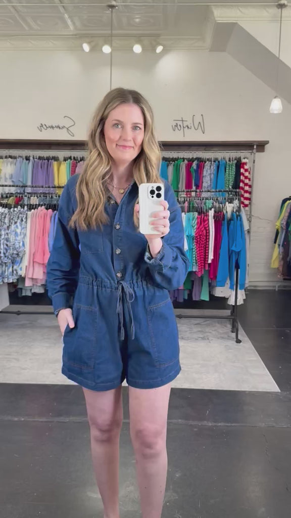 Woman wearing a denim romper that is collared with a tie waist and pockets.