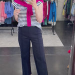 Woman wearing a striped blue and white top with a hot pink cardigan over her shoulders and navy pants. 